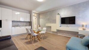 A modern kitchen with white cabinets, a glass dining table, and a flat-screen TV mounted on the wall. - The house of the badger (Feriolo)