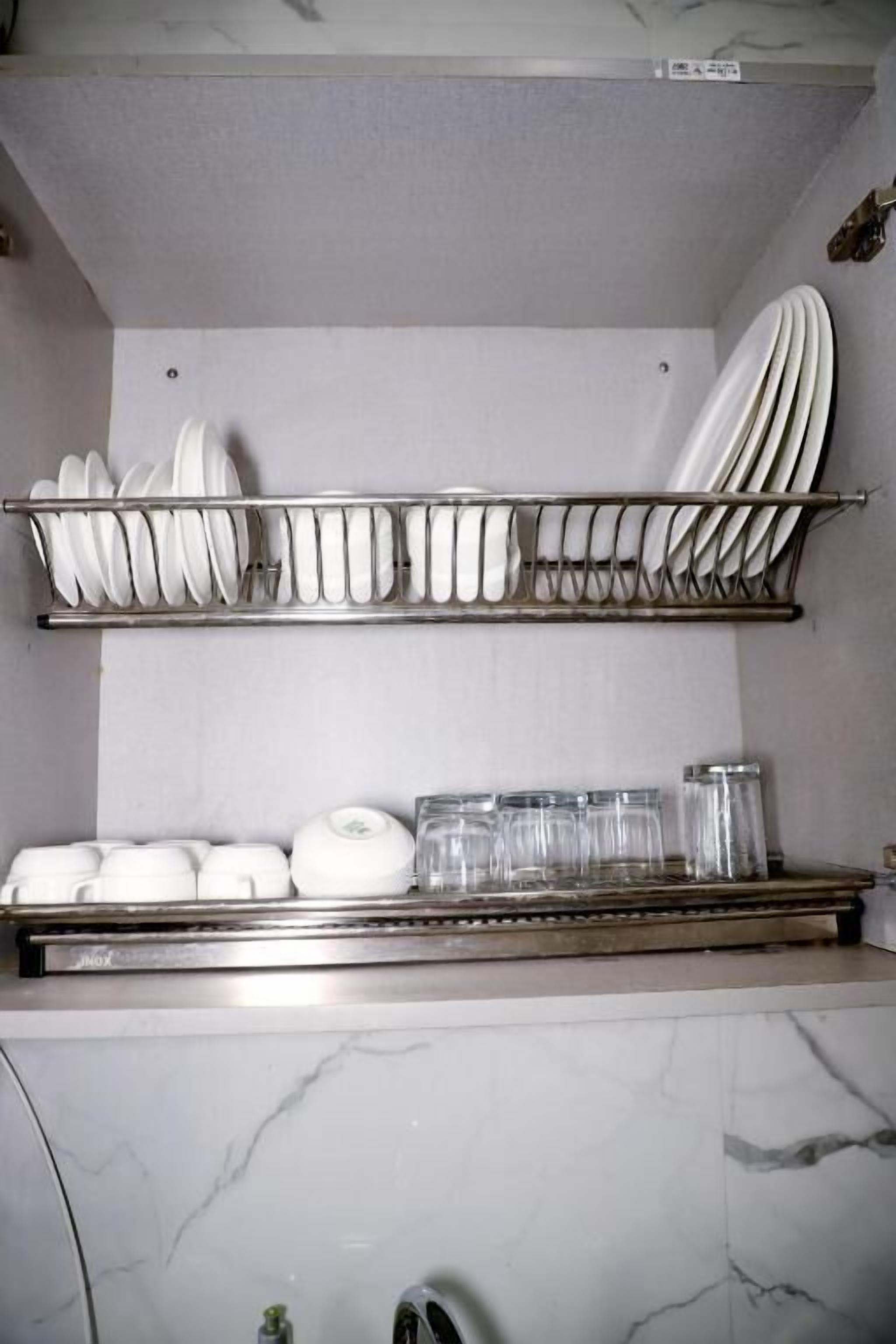 A kitchen with a marble countertop, a dish rack with plates, bowls, and glasses, and a stainless steel range hood.