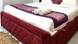 Un lit bien fait, avec une tête de lit rouge, du linge de lit blanc et un élément décoratif violet.