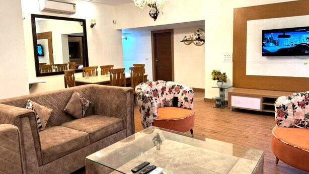 Un salon comprenant un canapé, deux fauteuils, une table basse en verre, un téléviseur et, au fond, un coin repas.