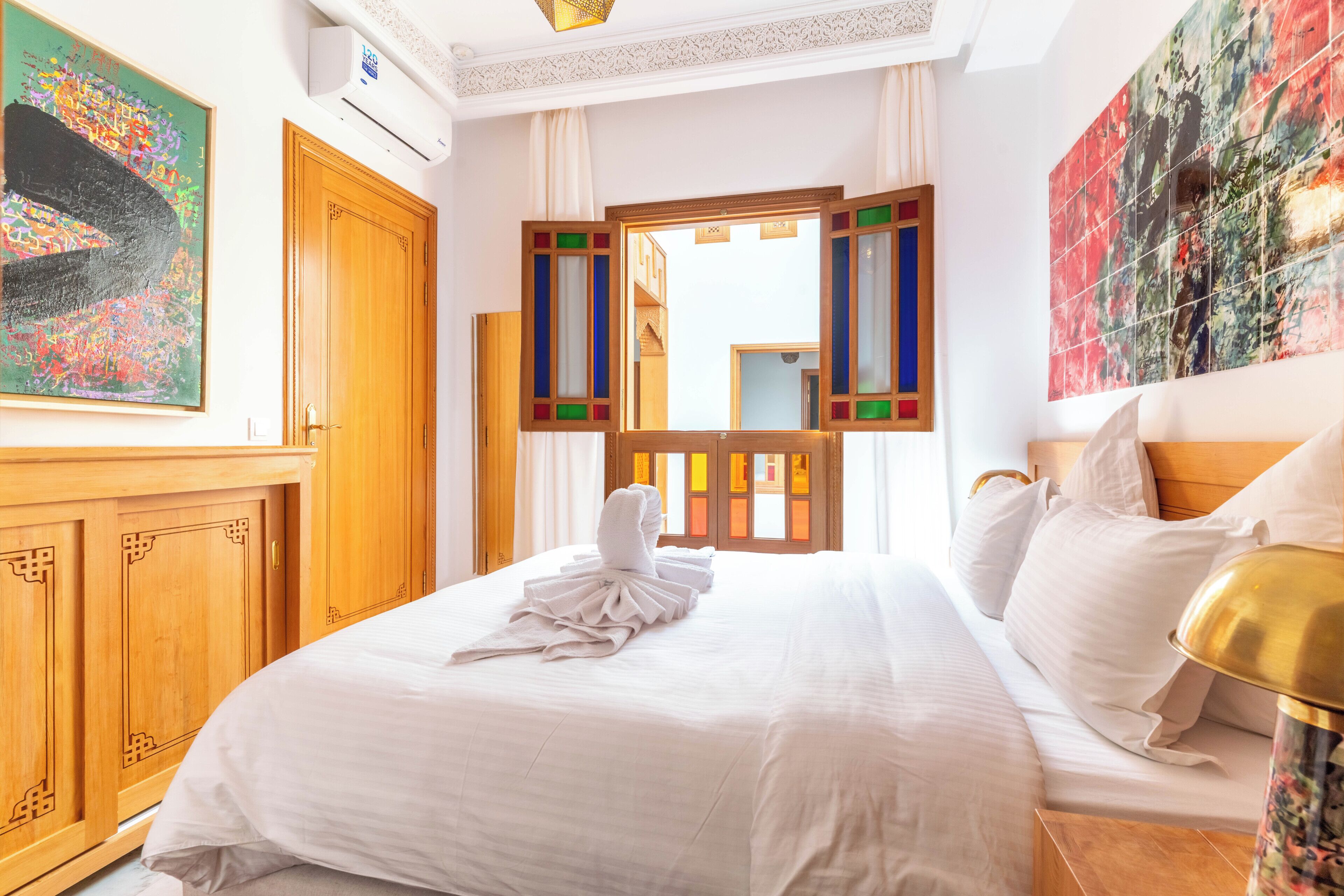 Una habitación de hotel con una cama, un armario de madera, un espejo y obras de arte en las paredes.