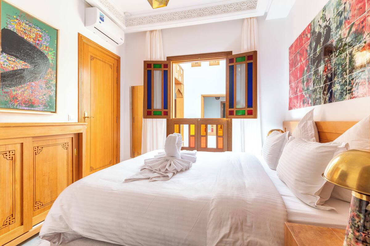 A hotel room with a bed, a wooden wardrobe, a mirror, and artwork on the walls.