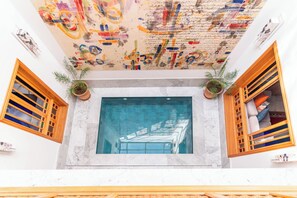 Un vestíbulo de hotel con un amplio ventanal, contraventanas de madera y un techo decorado con arte abstracto de colores.