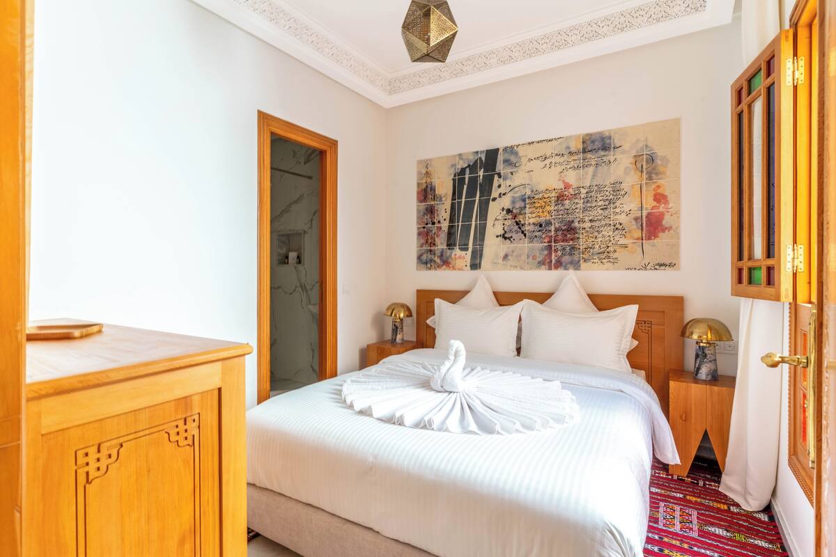 A hotel room with a bed, a wooden nightstand, a wall art piece, and a door.
