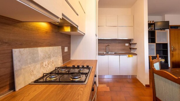 Een moderne keuken met een gasfornuis, houten keukenkastjes en een betegelde spatwand.
