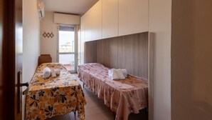 Een hotelkamer met twee bedden, een tafel met een bloemrijk tafelkleed, een wandairconditioner en een raam met uitzicht.