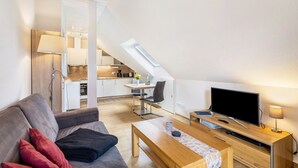 A modern living room with a sofa, a coffee table, a TV, and a dining area with a table and chairs. - Holiday Apartment for 2 People (45 m²) in Bad Arolsen (Bad Arolsen)