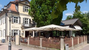 Restaurante com mesas ao ar livre, varanda e placa com a inscrição 'Schlossgarten'.
