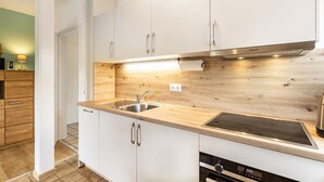 Uma cozinha moderna com armários brancos, bancada de madeira, pia de aço inoxidável e forno embutido.
