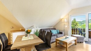 Um interior moderno com uma mesa de jantar, cadeiras, um sofá e uma varanda com vista para vegetação.