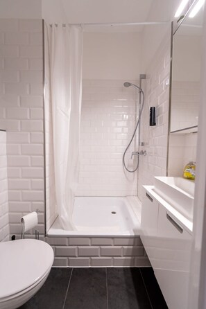A bathroom with a shower, toilet, and a sink with a mirror. - Apartment 2 Hamburg Winterhude (Hamburg)