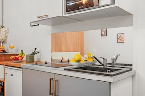 A modern kitchen with a built-in oven, a sink, and a wooden panel wall. - Chic Studio Near Champs-Elysees & Eiffel Tower (Paris)