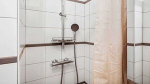 Suihkussa on käsisuihkupää, seinään asennettu hana ja ohjauspaneeli.