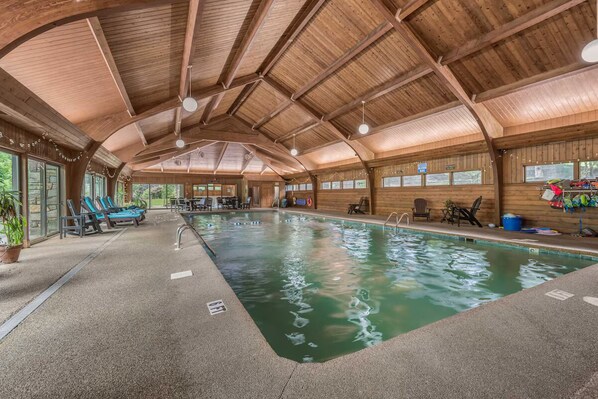 An indoor swimming pool with wooden beams, lounge chairs, and a view of the outdoors.