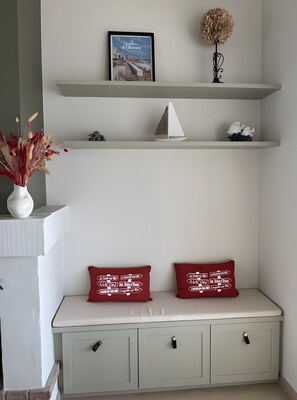 A seating area with a bench, two red cushions, a framed picture, a decorative plant, and a small sailboat model.