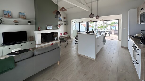Een ruime keuken met een centraal kookeiland, een eetgedeelte met uitzicht, en een woonkamer met een bank en televisie.