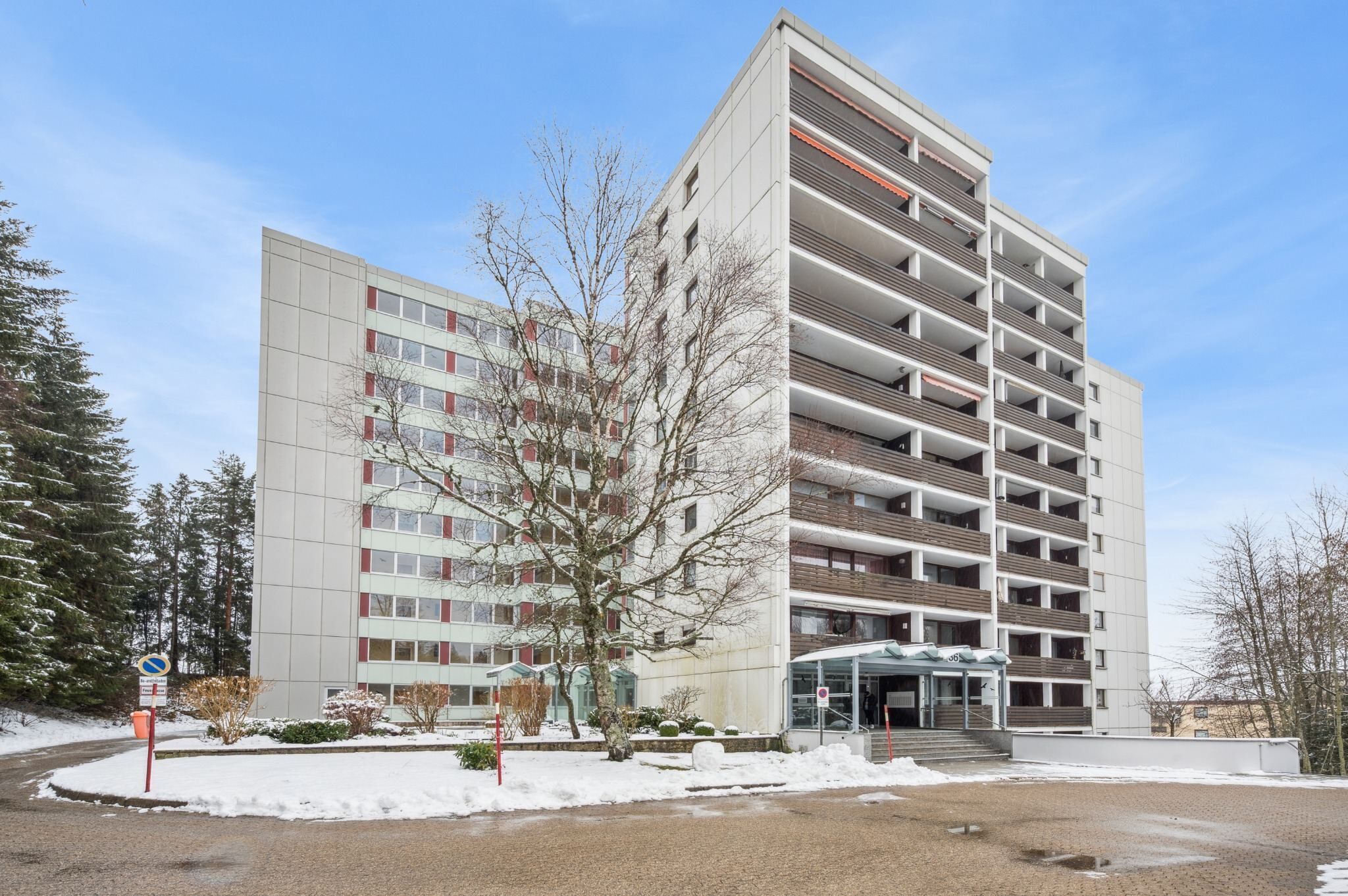 Ein mehrstöckiges Hotel mit modernem Design, das einen zentralen Eingang, Balkone und einen Parkbereich bietet.