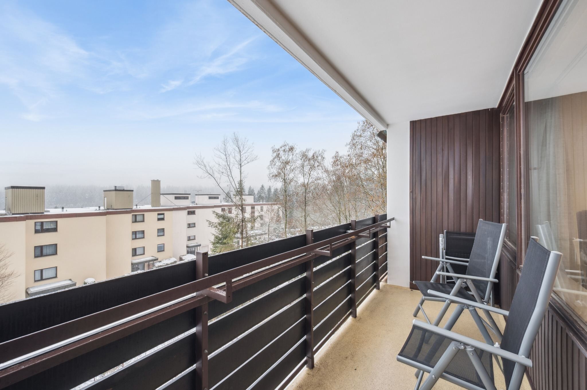 Un balcón con vista a edificios, una barandilla y una silla.