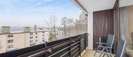 A balcony with a view of buildings, a railing, and a chair.