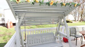 Une balançoire extérieure blanche, avec un banc en dessous, entourée d’une balustrade blanche et décorée de tournesols.
