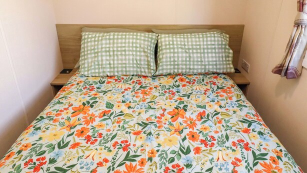 Un lit avec une couvre-lit à motifs floraux, deux coussins à carreaux et une tête de lit en bois.