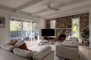 Ein Wohnzimmer mit Kamin aus Backsteinen, einem Fernseher und einem großen Fenster mit Blick auf eine Terrasse.