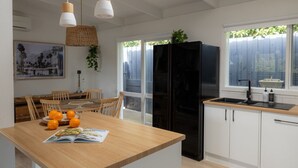 A modern kitchen with a black refrigerator, wooden dining table, and a window with a view of greenery. - Lovely Beach Cottage Heart of Rye (Rye)