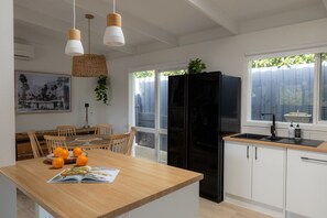 Eine moderne Küche mit einem schwarzen Kühlschrank, einem Holzes Esstisch und einem Fenster mit Blick auf Grünflächen.