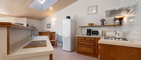 A kitchen with a wooden ceiling, a white refrigerator, a microwave, and a gas stove.