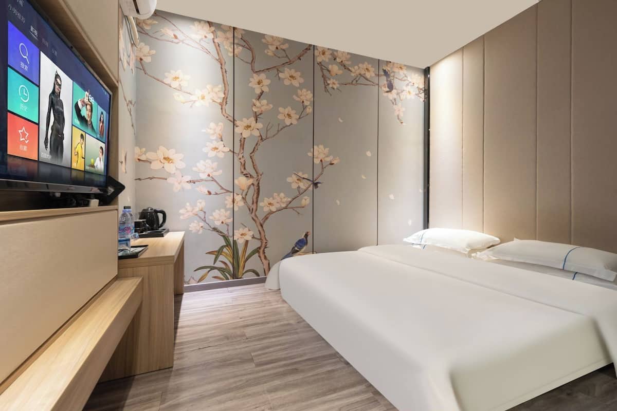 Quarto de hotel moderno com uma cama, uma escrivaninha, uma televisão e uma parede com um mural floral.