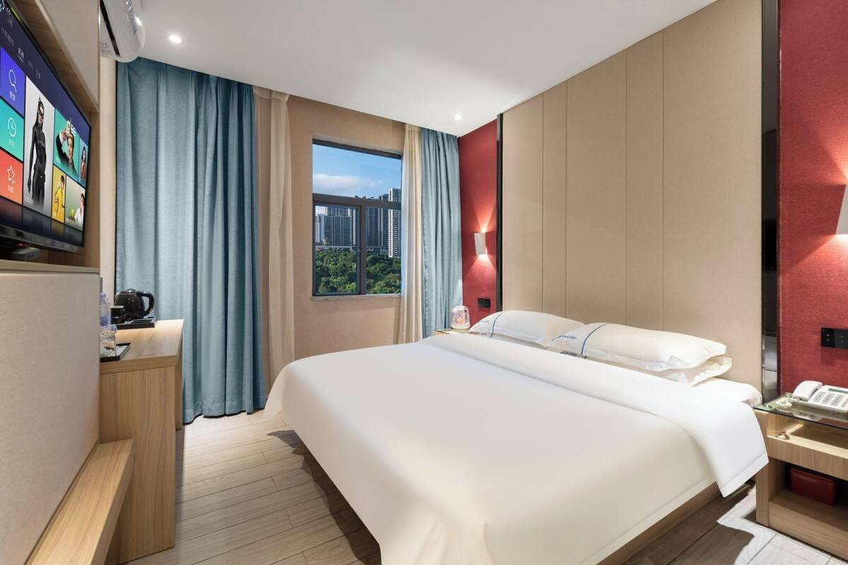Quarto de hotel com cama, televisão, escrivaninha com chaleira, telefone e janela com vista para a cidade.