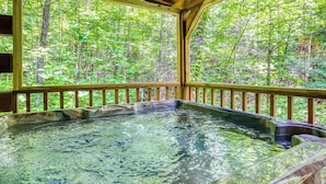 A hot tub with a wooden deck and large windows overlooking a forest. - Nestled Inn | Gated Forest Retreat | Hot Tub + 2 Jacuzzi Baths | Fireplace | (Sevierville)