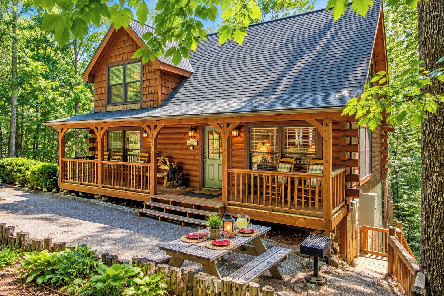 A log cabin with a porch, outdoor seating, and a grill area.