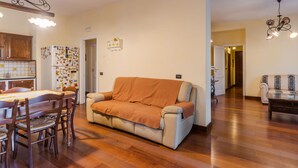 Ein Wohnzimmer mit Sofa, einem Esstisch mit Stühlen, einer Küchenzeile inklusive Schränken und Kühlschrank sowie einem Flur, der zu einem weiteren Raum führt.