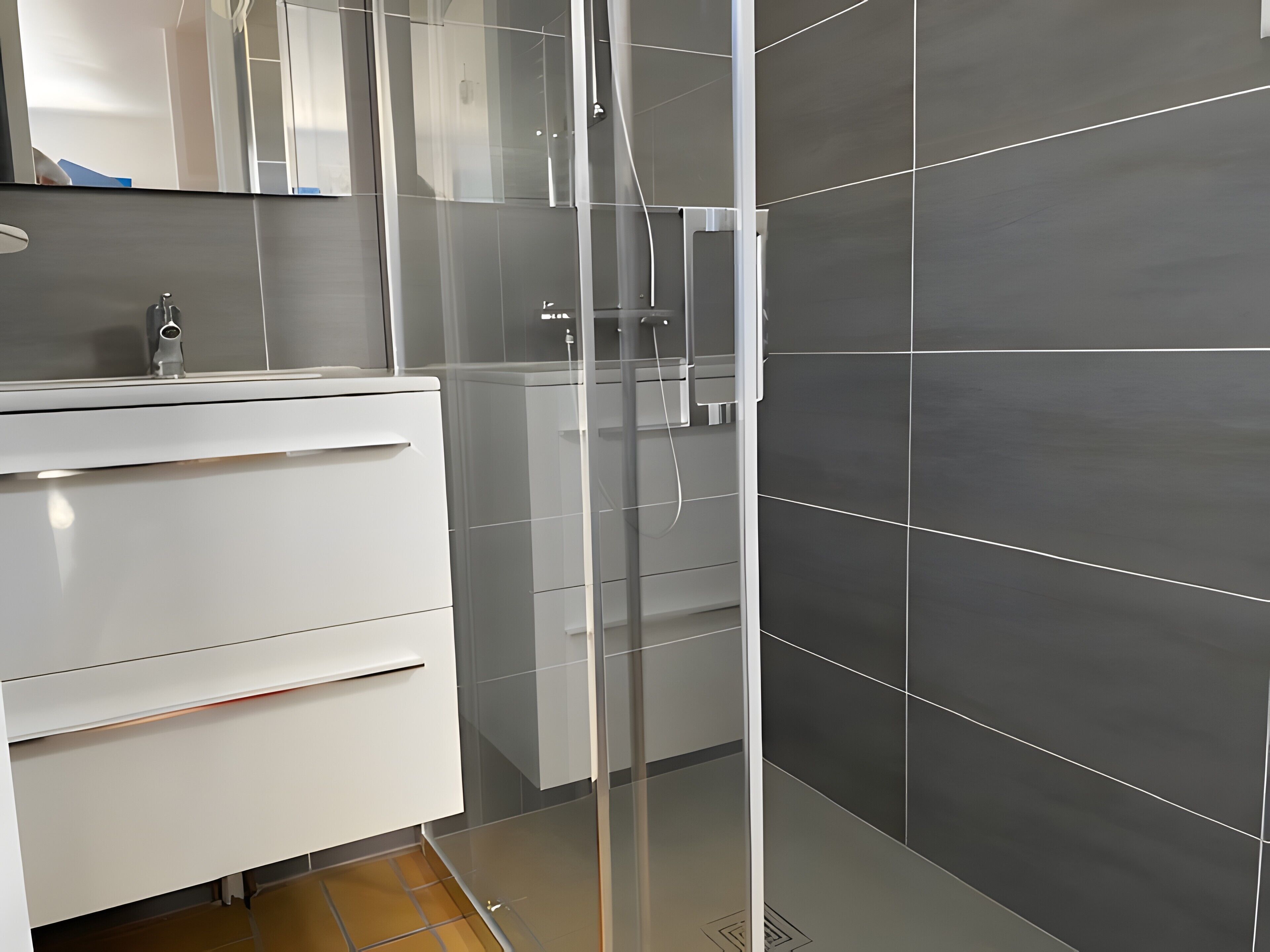 A modern bathroom with a glass shower enclosure, a white vanity, and dark tiled walls.