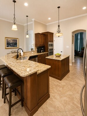 A kitchen with granite countertops, wooden cabinets, stainless steel appliances, and a central island with stools. - Spacious 4BR Retreat | Sleeps 8 • 2 Kings + 2 Queens (Corpus Christi)