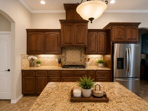 Eine Küche mit Holzausstattung, einem Edelstahl-Kühlschrank, Granit-Arbeitsplatten und einer zentralen Kochinsel mit Kerze und Pflanze.