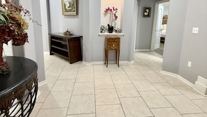 Un couloir doté d’un sol carrelé, un vase décoratif rempli de fleurs, un tableau encadré accroché au mur et une petite table sur laquelle sont posés un vase et une théière.