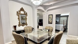 Un coin repas avec une table à plateau en verre, entourée de chaises à motifs, un lustre et un miroir décoratif accroché au mur.