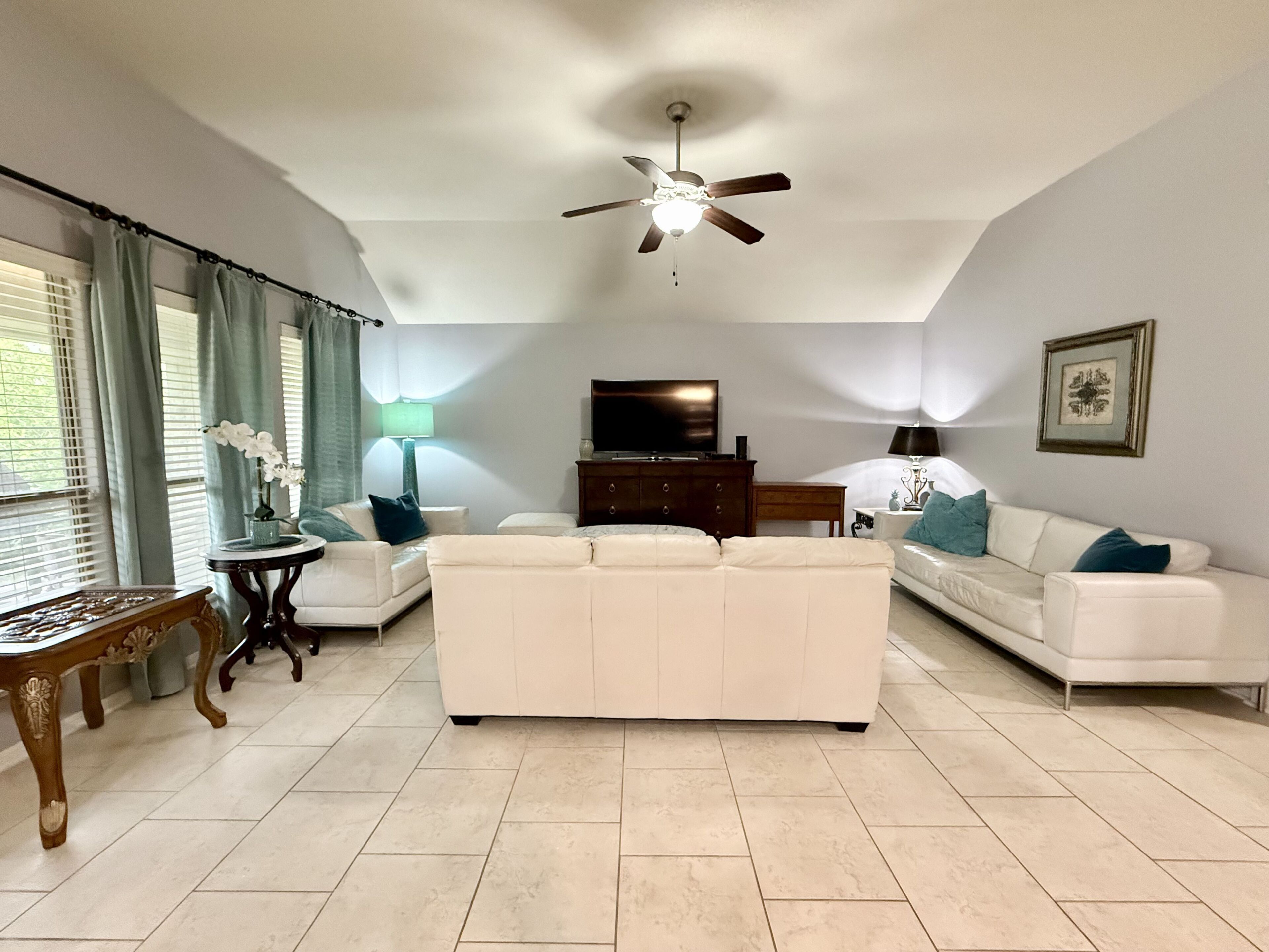 A living room with a ceiling fan, white sofas, a TV, and a table with a lamp.
