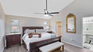 Ein Schlafzimmer mit Bett, Nachttischen, einer Bank, einem Deckenventilator, einem Spiegel und einem begehbaren Kleiderschrank.