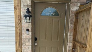 A brown door with a glass panel, a wooden post, a black lantern, and a welcome mat. - Spacious Southside Home 1 King & 1 Queen bed! (Corpus Christi)