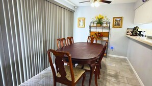 A dining area with a round table, chairs, a ceiling fan, and a window with blinds. - Spacious Southside Home 1 King & 1 Queen bed! (Corpus Christi)