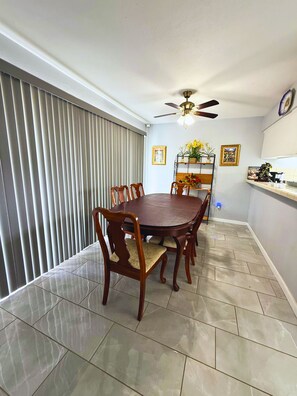 A dining area with a round table, chairs, a ceiling fan, and a window with blinds. - Spacious Southside Home 1 King & 1 Queen bed! (Corpus Christi)