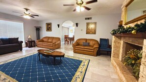 A living room with a blue patterned rug, two leather sofas, a coffee table, a fireplace, and two ceiling fans. - Spacious Southside Home 1 King & 1 Queen bed! (Corpus Christi)