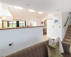 A spacious living area with a high ceiling, a wooden staircase, and a view of the outdoors through large windows. - Storytellers at Isay | Luxe Skye Coastal Stay (Waternish)