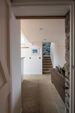 A hallway with a staircase, a stone wall, and a brown sofa. - Storytellers at Isay | Luxe Skye Coastal Stay (Waternish)
