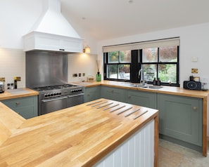 A modern kitchen with a central island, a stove, and a window with a view of the outdoors. - Storytellers at Isay | Luxe Skye Coastal Stay (Waternish)