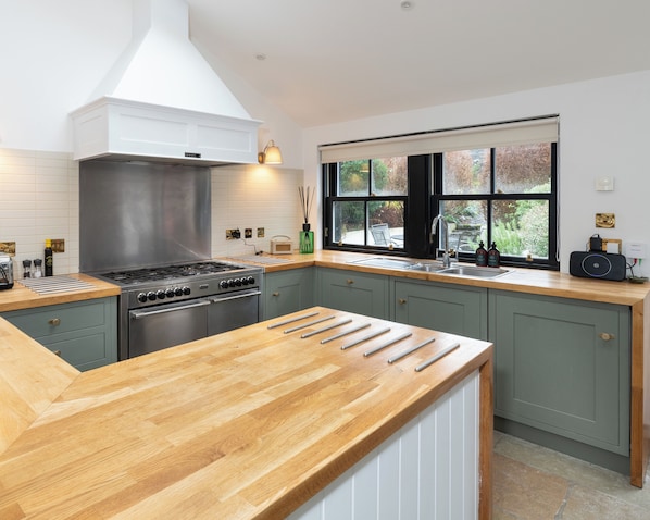 A modern kitchen with a central island, a stove, and a window with a view of the outdoors. - Storytellers at Isay | Luxe Skye Coastal Stay (Waternish)