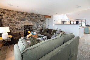 A cozy living room with a stone wall, a fireplace, a sofa, and a coffee table. - Storytellers at Isay | Luxe Skye Coastal Stay (Waternish)